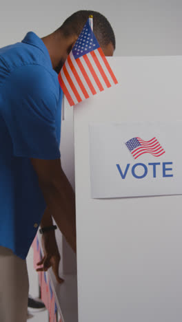 Vertical-Video-Shot-Of-Man-Walking-Into-Booth-With-Ballot-Paper-To-Cast-Vote-In-American-Election---Shot-In-Slow-Motion